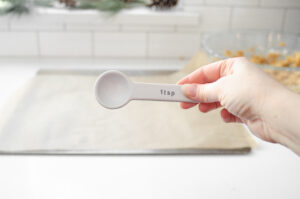 A hand holding a white teaspoon measuring spoon.