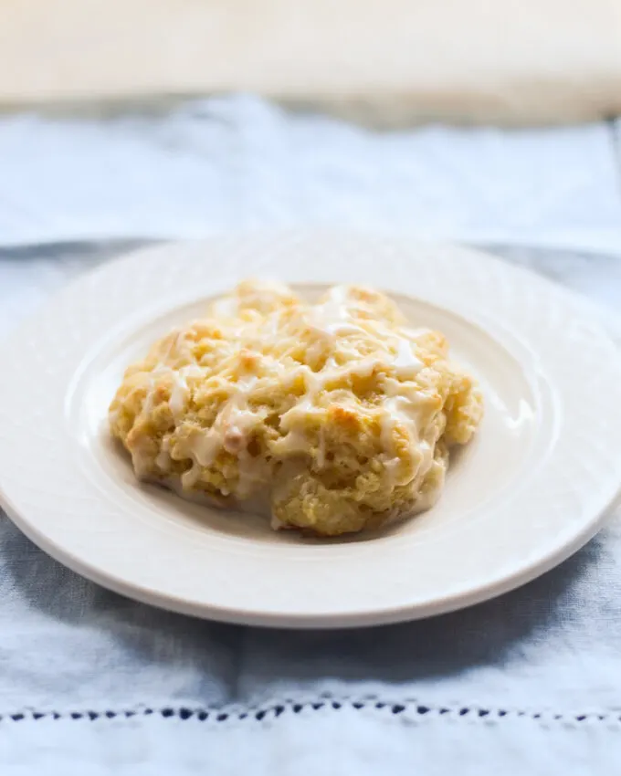 An orange scone on a white plate on top of blue napkin.