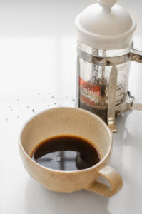 Espresso strength coffee in a mug with a French press behind it.
