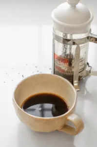 Espresso strength coffee in a mug with a French press behind it.