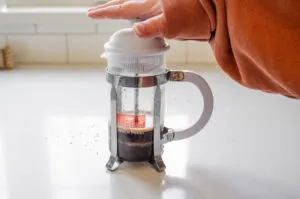 Plunging down the French press after it has been allowed to sit for 4 minutes.
