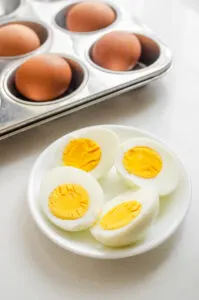 A bowl of baked hard boiled eggs with a muffin tin with whole eggs behind it.