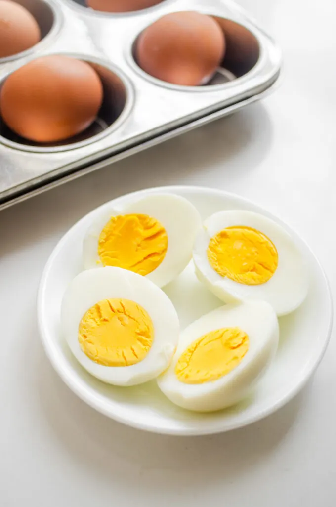 A bowl of baked hard boiled eggs with a muffin tin with whole eggs behind it.