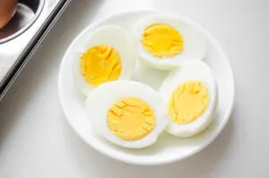 A bowl of baked hard boiled eggs with a muffin tin with whole eggs beside it.