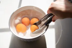 Placing the baked hard boiled eggs into a bowl of ice water.