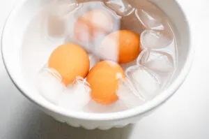 The baked hard boiled eggs in a bowl of ice water.