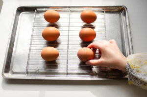 Placing whole brown eggs on a wire rack on top of a baking sheet.