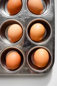 A vertical photo of a muffin tin with baked whole eggs inside.