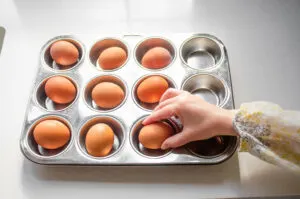 Placing eggs into a muffin tin to make baked hard boiled eggs.