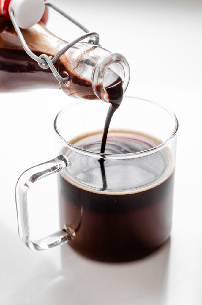 Pouring chocolate syrup into a mug of coffee.