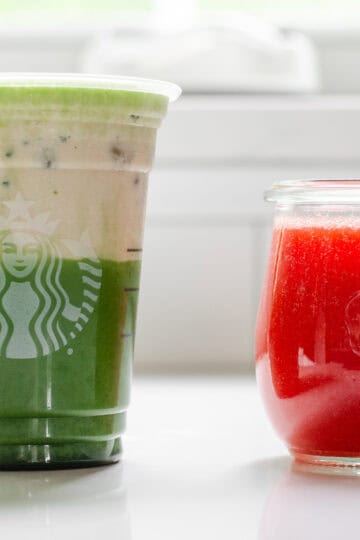 A jar of homemade Starbucks strawberry puree sauce next to a Starbucks glass filled with an iced matcha latte and strawberry cold foam on top.