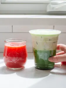 A jar of homemade Starbucks Strawberry Puree with a Starbucks glass filled with a matcha latte with strawberry sweet cream on top.