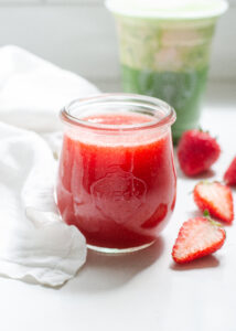 A jar of homemade Starbucks strawberry puree on a white countertop with fresh strawberries beside it.