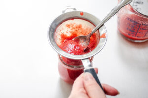 Running the strawberry puree through a fine mesh sieve to remove the seeds.