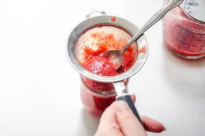 Running the strawberry puree through a fine mesh sieve to remove the seeds.
