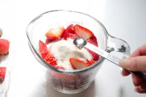 Adding the sugar and strawberry flavoring to the fresh strawberries.