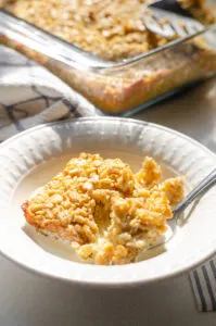 A bowl of baked oatmeal with cream on top and the pan in the background.