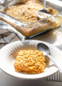 A bowl of baked oatmeal with the pan in the background and a spoon off to the side.
