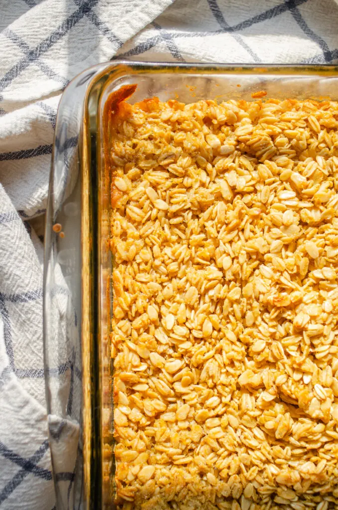 The finished baked oatmeal in the pan on a white countertop with a checked dish towel off to the side.