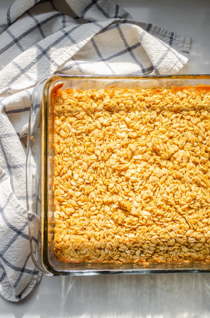 The finished baked oatmeal in the pan on a white countertop with a checked dish towel off to the side.