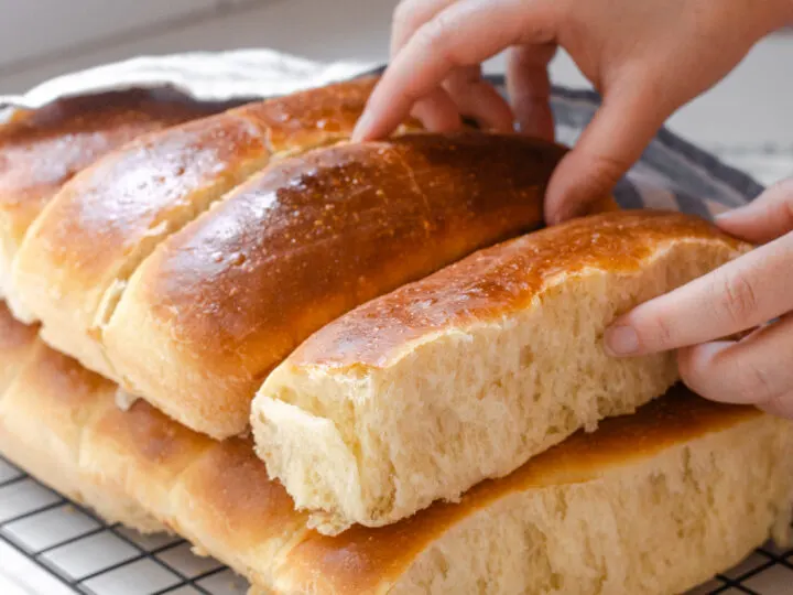 A stack of homemade sourdough hotdog buns on a black wire cooling rack with a linen napkin off to the side.