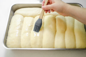 Brushing the risen hotdog buns with an egg wash.