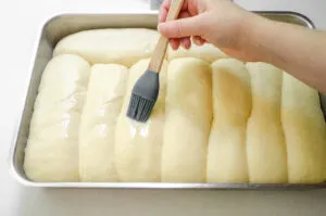 Brushing the risen hotdog buns with an egg wash.