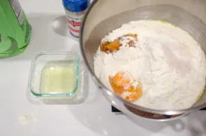 A stand mixer with the dough ingredients in it, with the extra egg white in a small glass container off to the side.