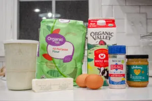 All of the ingredients needed to make sourdough hotdog buns laid out on a white countertop. 
