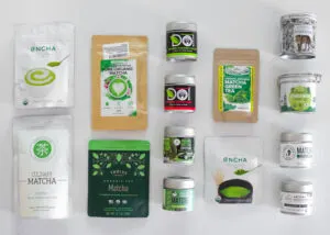 14 different brands of matcha powders on a white countertop. 