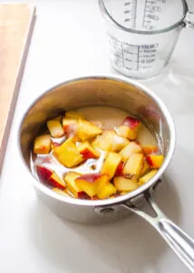 A pan with peaches, water, and sugar inside.