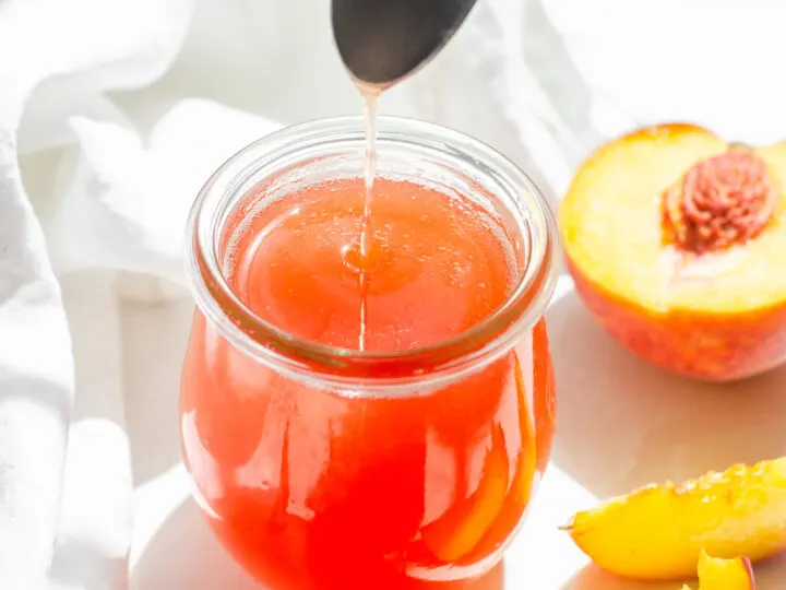 Peach syrup in a jar with fresh peaches and a white napkin around it.