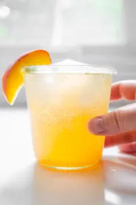 A peach mocktail in a Weck jar with a fresh peach slice on the side.