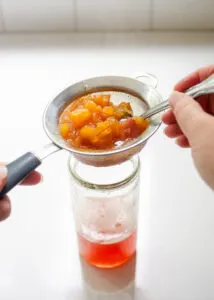 Straining the peach syrup through a fine mesh sieve.