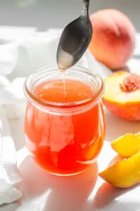 Peach syrup in a jar with fresh peaches and a white napkin around it.