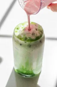 Pouring the strawberry cold foam on top of the iced matcha latte.