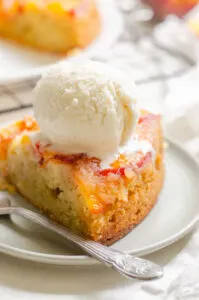 A slice of peach olive oil cake on a grey plate with a scoop of ice cream on top.