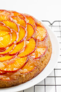 A peach olive oil cake on a serving plate on a wire cooling rack.