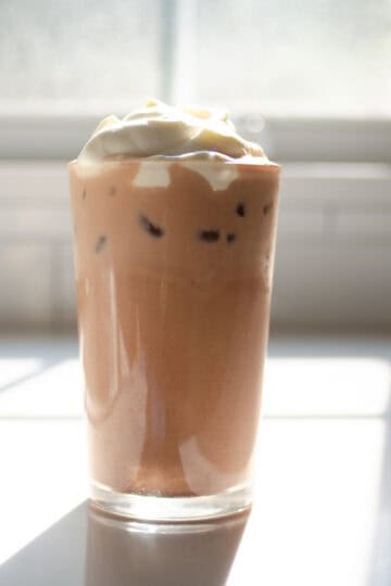 A glass of homemade Starbucks mocha iced latte on a sunny white countertop.