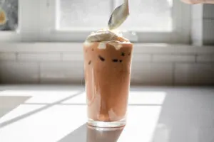 Dolloping the whipped cream on top of the iced mocha.