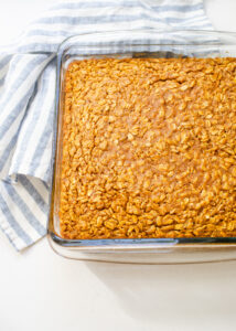 A pan of pumpkin pie baked oatmeal on a white countertop with a blue and white striped linen napkin off to the side.