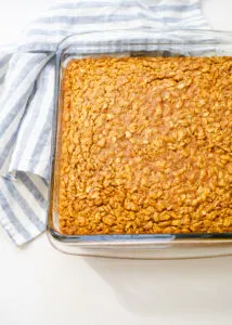 A pan of pumpkin pie baked oatmeal on a white countertop with a blue and white striped linen napkin off to the side.