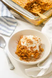 A bowl of pumpkin pie baked oatmeal with a dollop of maple whipped cream on top and the pan in the background.