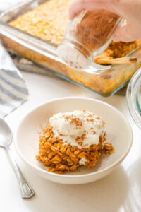 Sprinkling a bowl of pumpkin pie baked oatmeal with some pumpkin pie spice mix.