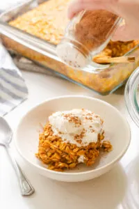 Sprinkling a bowl of pumpkin pie baked oatmeal with some pumpkin pie spice mix.
