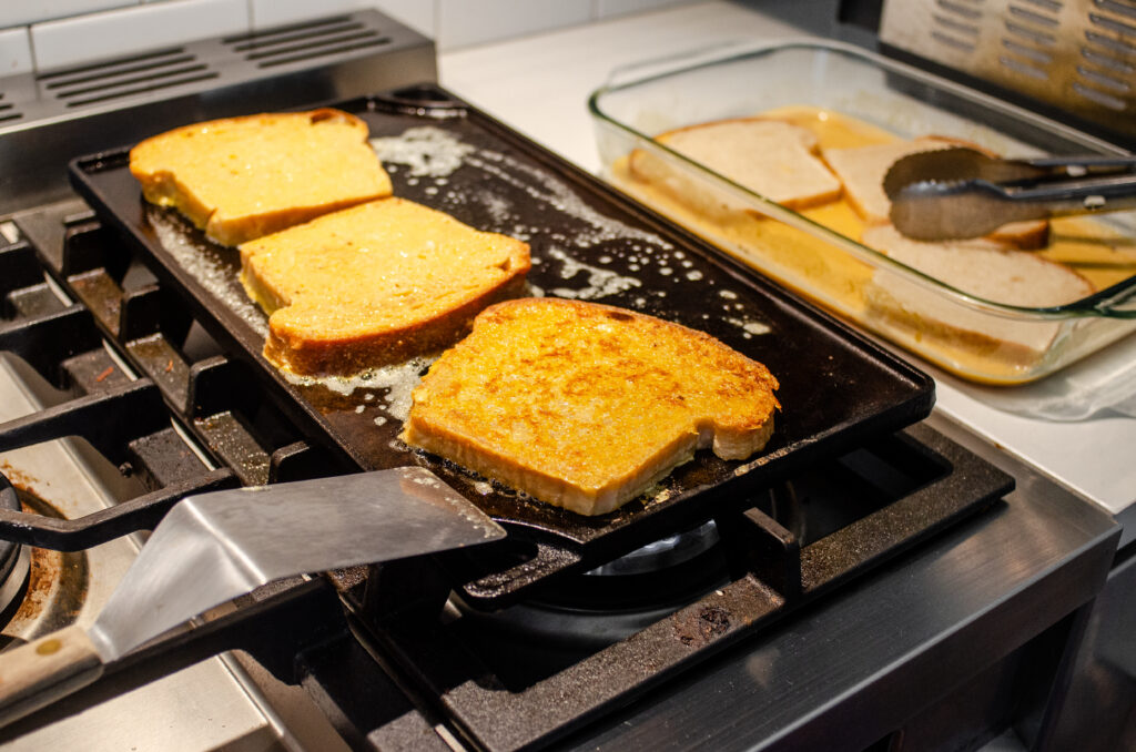 Slices of bread on a cast iron griddle with one slice flipped over.