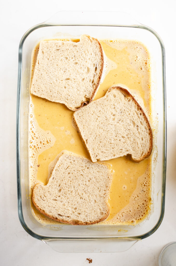 A 13x9 inch glass pan of pumpkin french toast custard with slices of sourdough bread soaking in it.