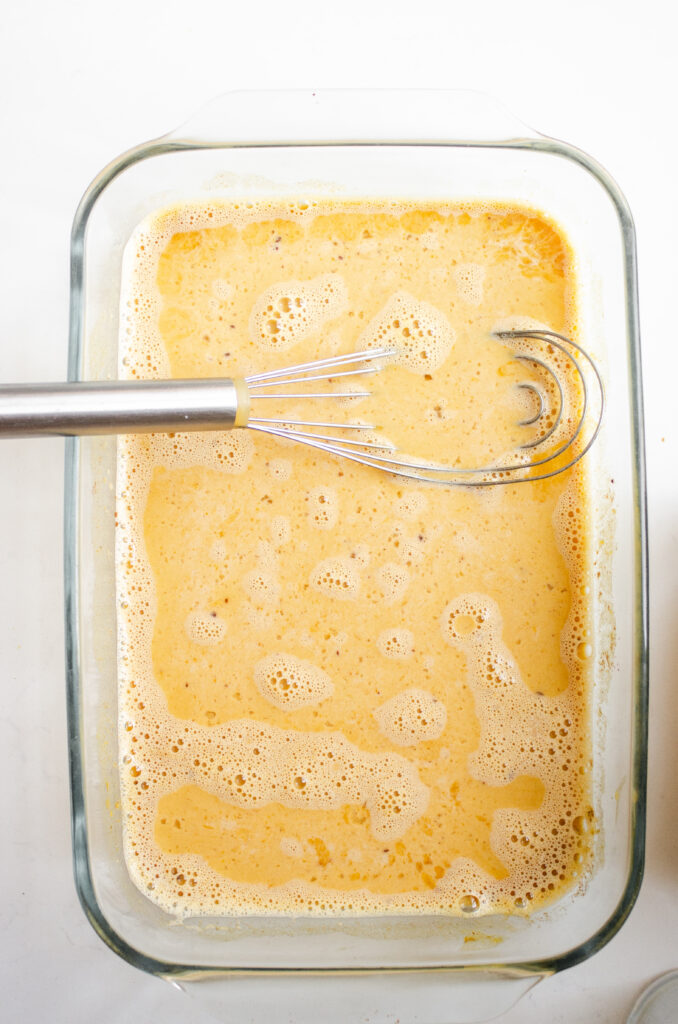A 13x9 inch pan with French toast custard and a whisk.