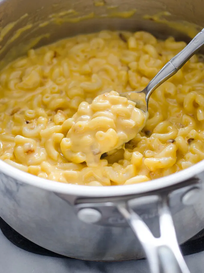 A spoonful of butternut squash mac and cheese held over the pot.