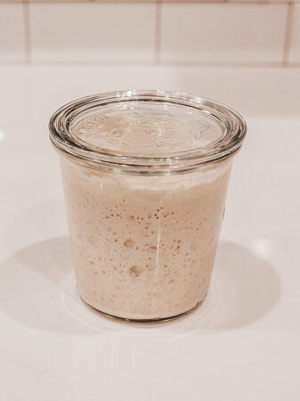 A bubbly sourdough starter in a Weck jar on a white countertop.